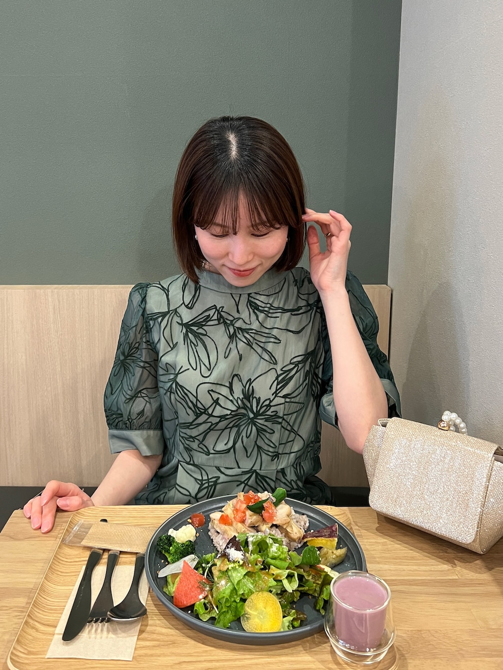 ゴールド系のハンドバッグ、ベージュ系のパンプス、グリーン系のドレスを着用したレディースの春コーディネートの5枚目の写真