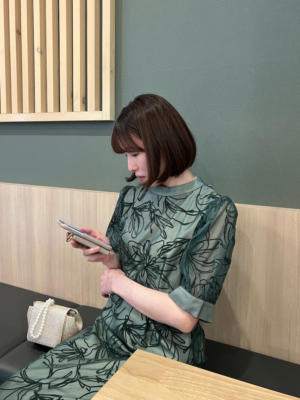 ゴールド系のハンドバッグ、ベージュ系のパンプス、グリーン系のドレスを着用したレディースの春コーディネートの4枚目の写真