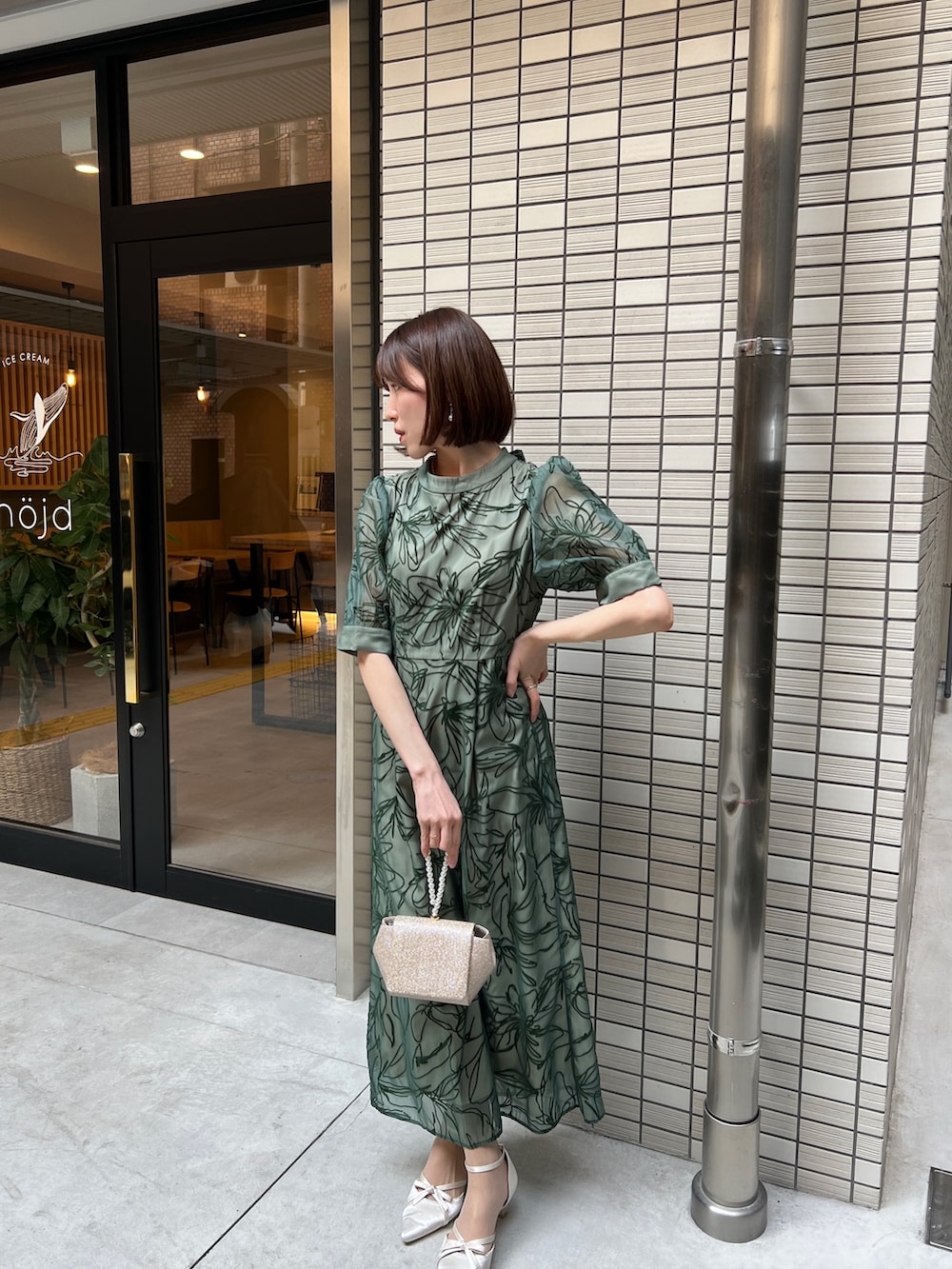 ゴールド系のハンドバッグ、ベージュ系のパンプス、グリーン系のドレスを着用したレディースの春コーディネートの2枚目の写真
