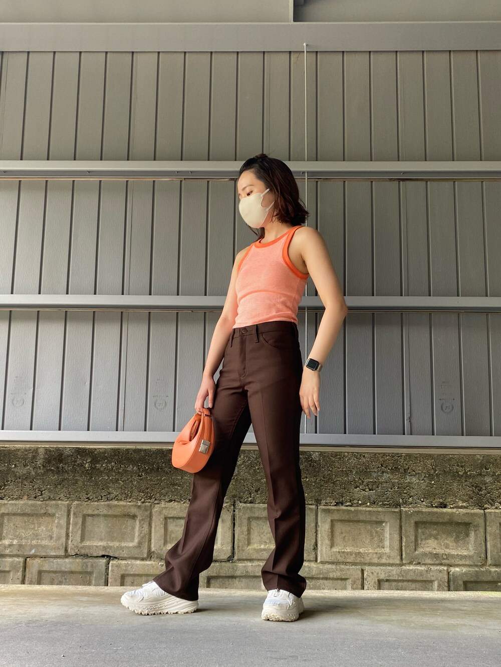 ブラウン系のスラックス、オレンジ系のハンドバッグ、オレンジ系のタンクトップを着用したレディースの夏コーディネートの3枚目の写真