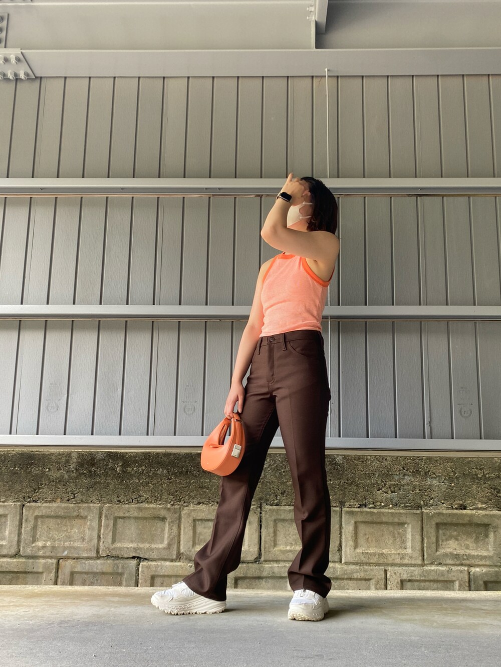 ブラウン系のスラックス、オレンジ系のハンドバッグ、オレンジ系のタンクトップを着用したレディースの夏コーディネートの2枚目の写真