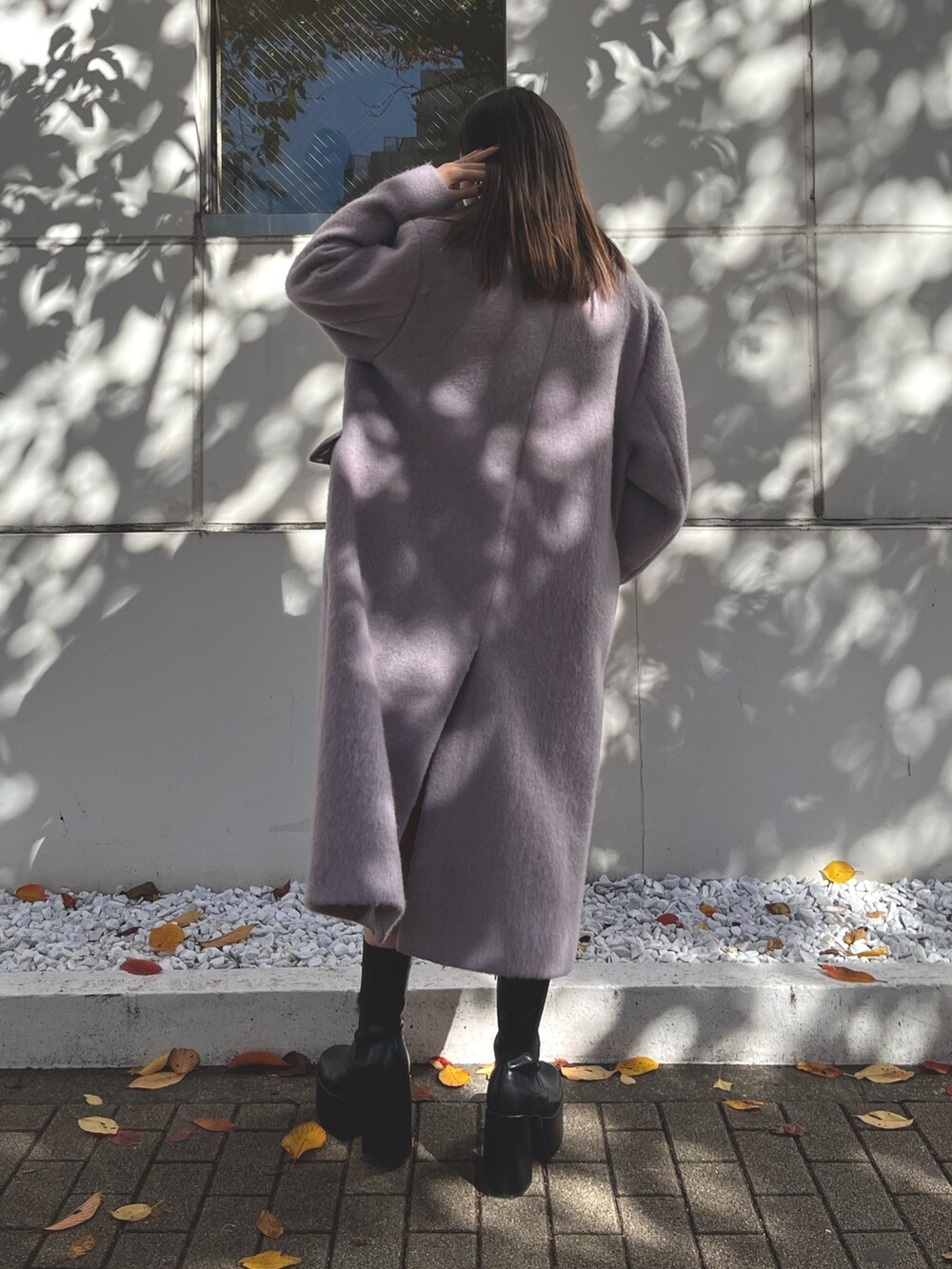 パープル系のチェスターコート、ブラック系のワンピース、ブラック系のブーツを着用したレディースの冬コーディネートの3枚目の写真