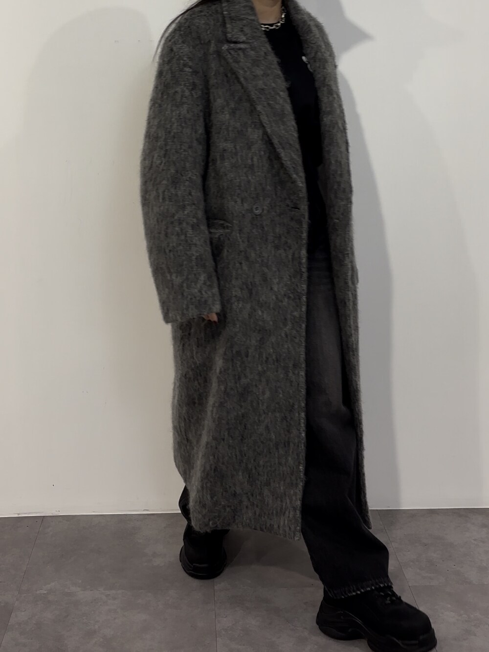 ブラック系のデニムパンツ、ブラック系のスニーカー、グレー系のチェスターコートを着用したレディースの冬コーディネートの2枚目の写真