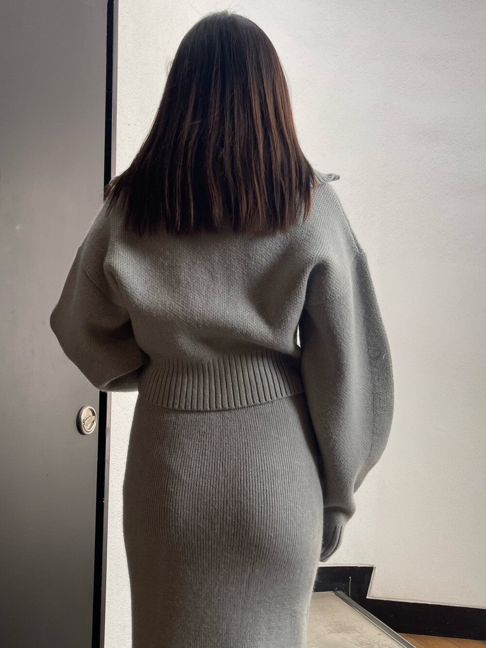 グレー系のニット/セーター、グレー系のスカート、ブラック系のブーツを着用したレディースの冬コーディネートの6枚目の写真