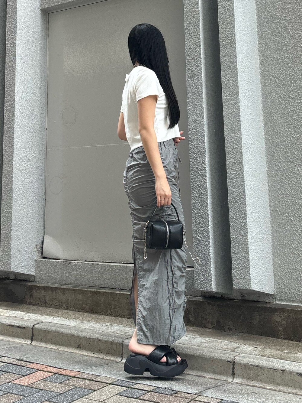 ブラック系のサンダル、ホワイト系のTシャツ/カットソー、ブラック系のハンドバッグを着用したレディースの夏コーディネートの2枚目の写真