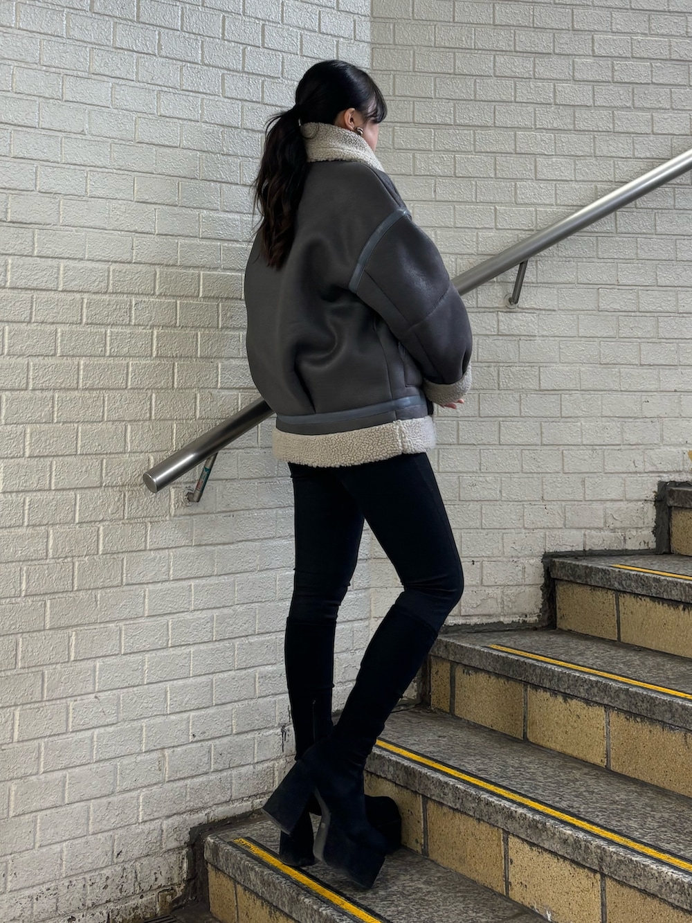 グレー系のムートンコート、ブラック系のデニムパンツ、その他のブーツを着用したレディースの秋コーディネートの2枚目の写真