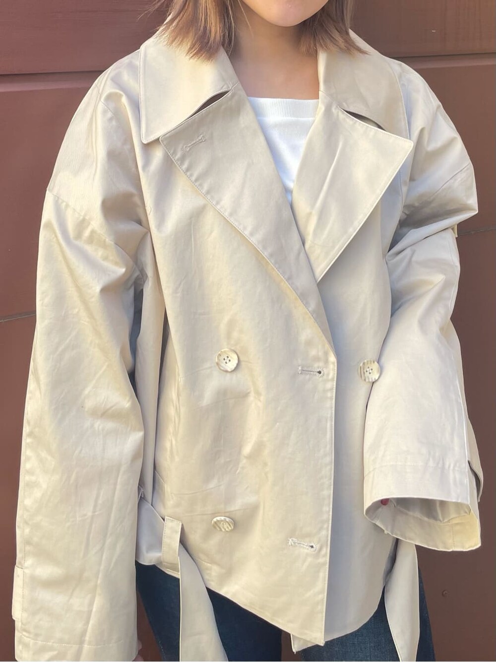 ベージュ系のトレンチコート、ブルー系のデニムパンツ、ブラック系のブーツを着用したレディースの冬コーディネートの2枚目の写真