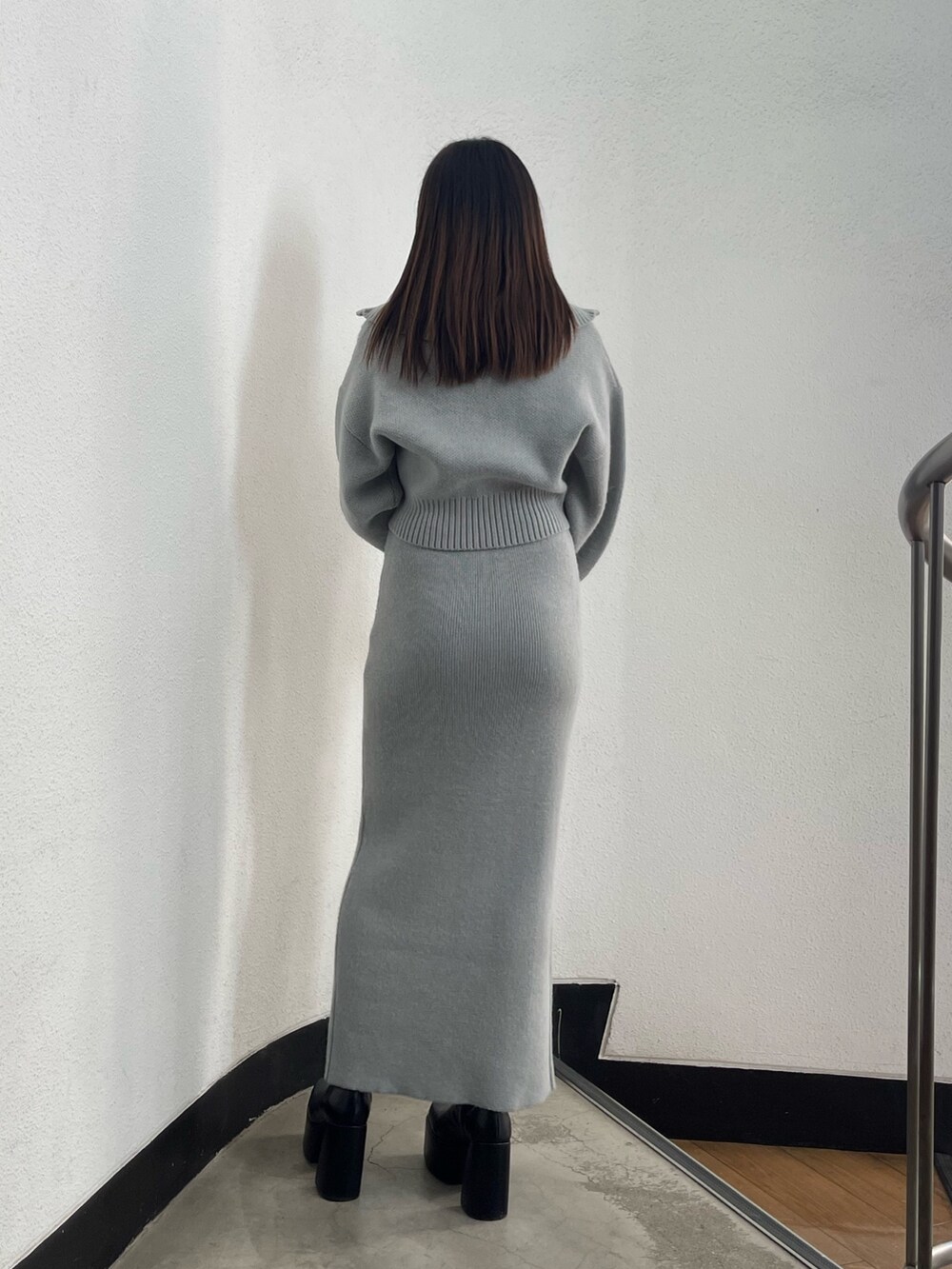 グレー系のニット/セーター、グレー系のスカート、ブラック系のブーツを着用したレディースの冬コーディネートの2枚目の写真