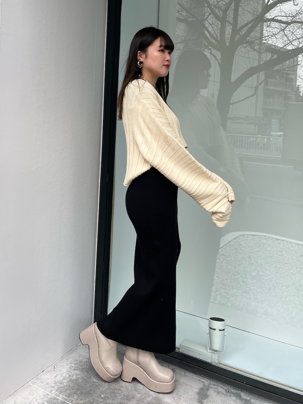 ホワイト系のニット/セーター、ベージュ系のブーツ、ブラック系のワンピースを着用したレディースの春コーディネートの2枚目の写真