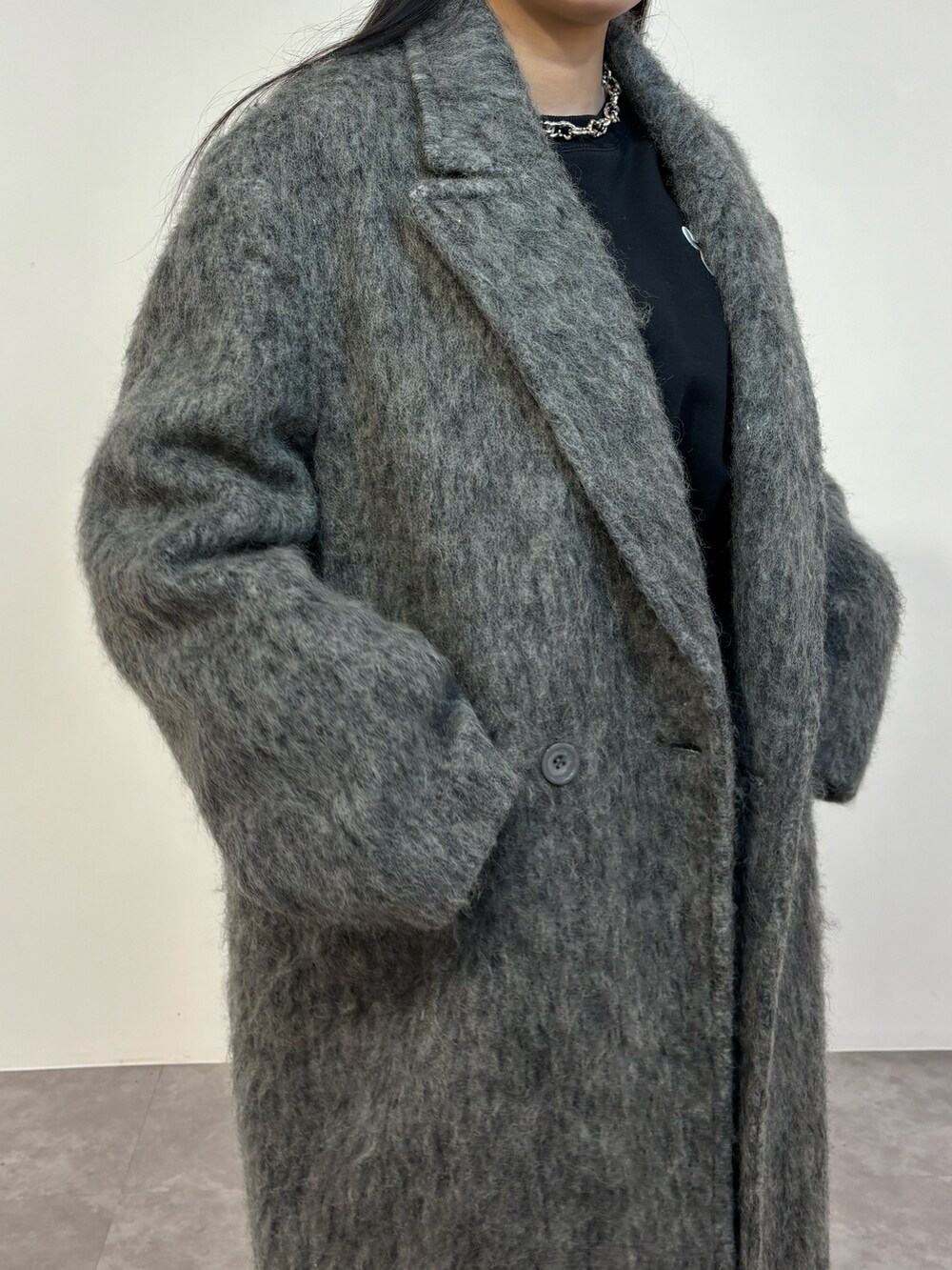 ブラック系のデニムパンツ、ブラック系のスニーカー、グレー系のチェスターコートを着用したレディースの冬コーディネートの3枚目の写真