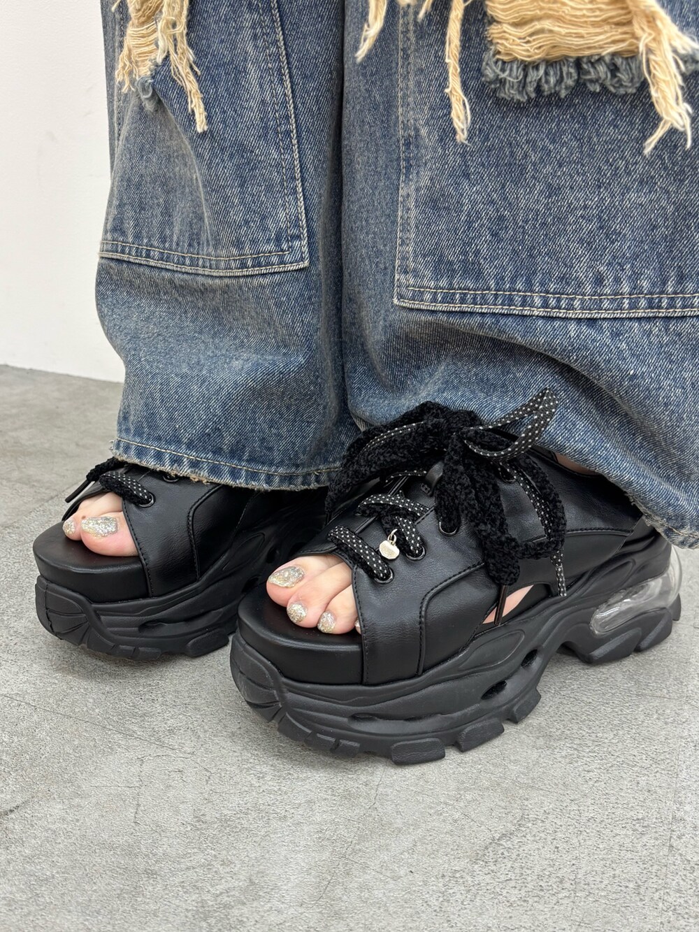 ブラック系のサンダル、ブルー系のデニムパンツを着用したレディースの春コーディネートの5枚目の写真