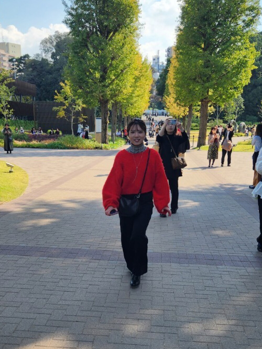 レッド系のニット/セーター、ブラック系のスラックス、ブラック系のショルダーバッグを着用したレディースの秋コーディネートの3枚目の写真