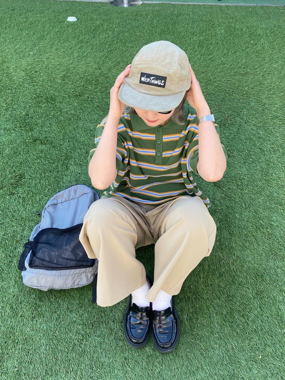 グレー系のスラックス、グリーン系のポロシャツ、ベージュ系のキャップを着用したレディースの春コーディネートの3枚目の写真