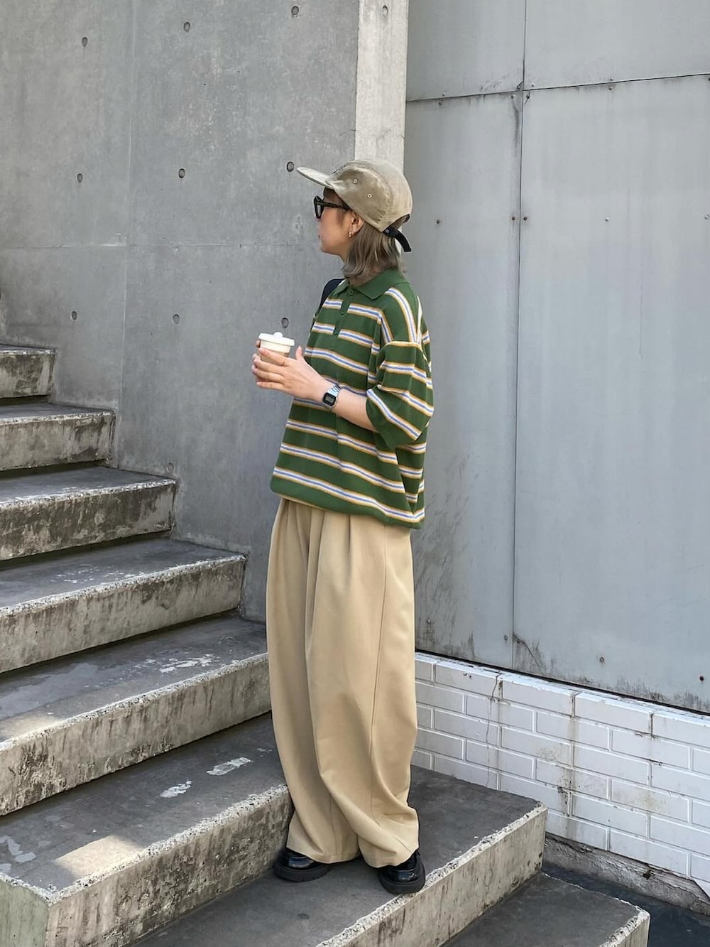 グレー系のスラックス、グリーン系のポロシャツ、ベージュ系のキャップを着用したレディースの春コーディネートの2枚目の写真