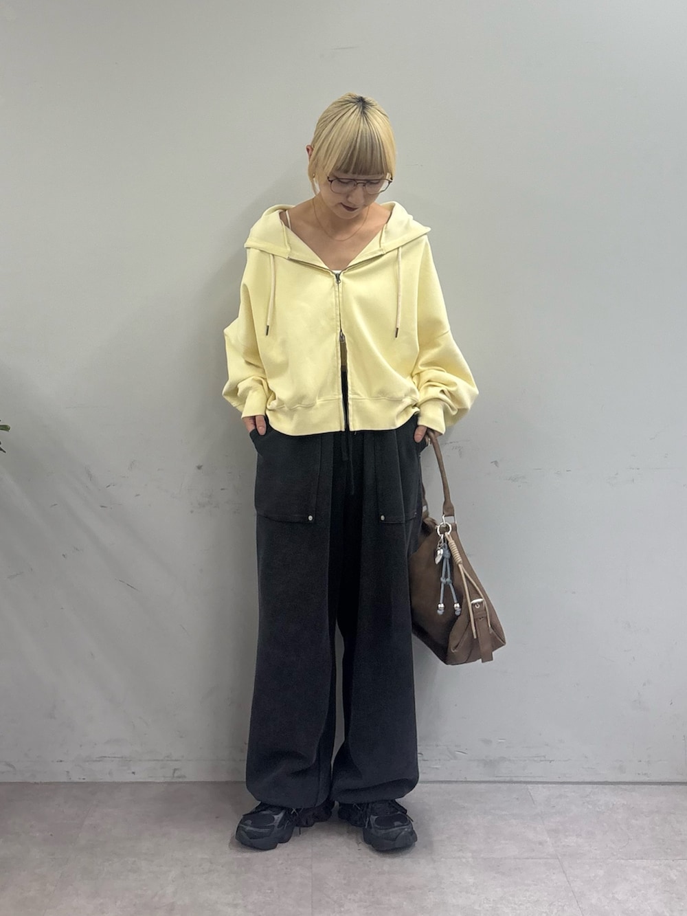 イエロー系のパーカー、ブラック系のスウェットパンツ、ベージュ系のトートバッグを着用したレディースの春コーディネートの2枚目の写真