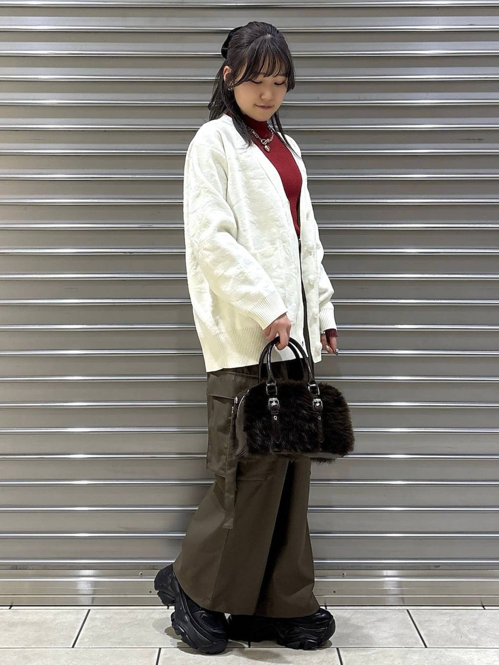 ブラック系のスニーカー、ブラウン系のスラックス、ホワイト系のカーディガン/ボレロを着用したレディースの冬コーディネートの2枚目の写真