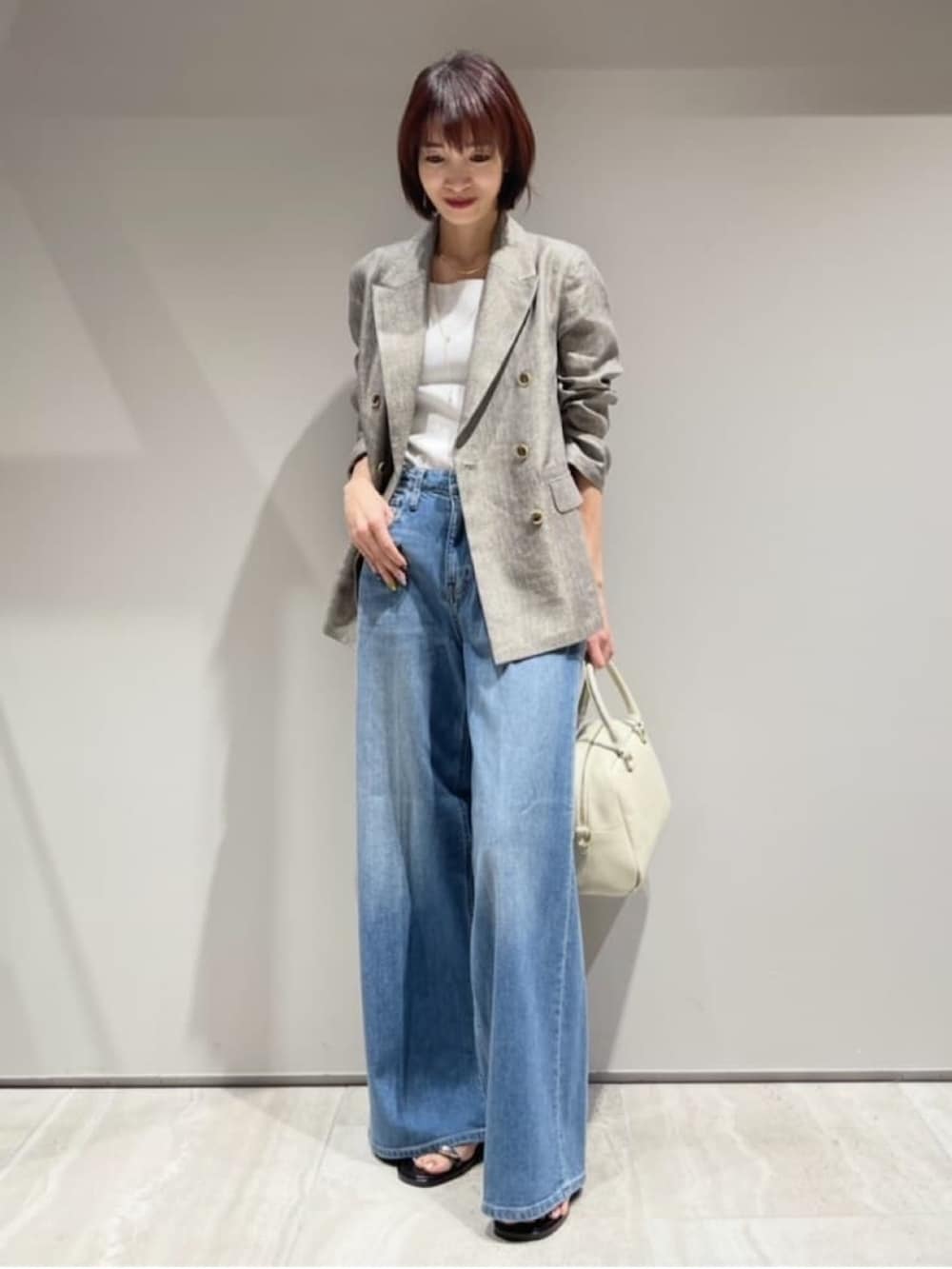 ブルー系のデニムパンツ、ベージュ系のテーラードジャケット、ホワイト系のタンクトップを着用したレディースの春コーディネートの2枚目の写真