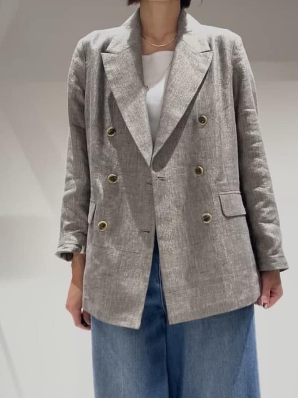 ブルー系のデニムパンツ、ベージュ系のテーラードジャケット、ホワイト系のタンクトップを着用したレディースの春コーディネートの4枚目の写真