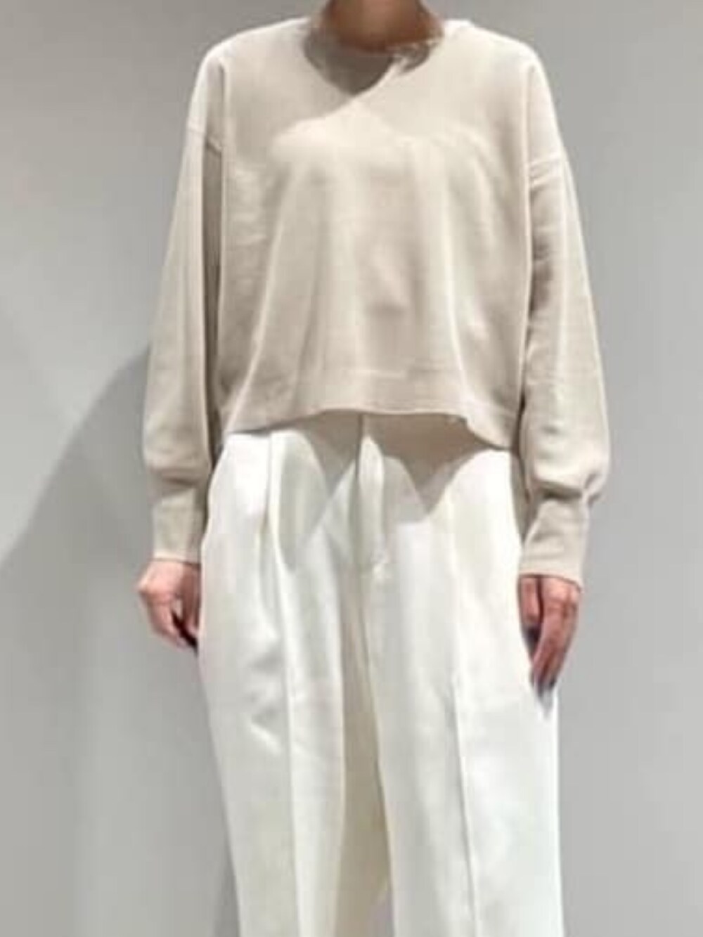 ベージュ系のニット/セーター、ホワイト系のスラックス、ゴールド系のネックレスを着用したレディースの秋コーディネートの2枚目の写真