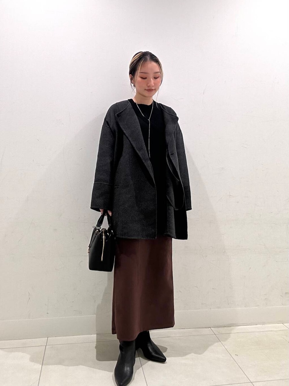 グレー系のノーカラーコート、ブラック系のハンドバッグ、ブラック系のニット/セーターを着用したレディースの冬コーディネートの3枚目の写真