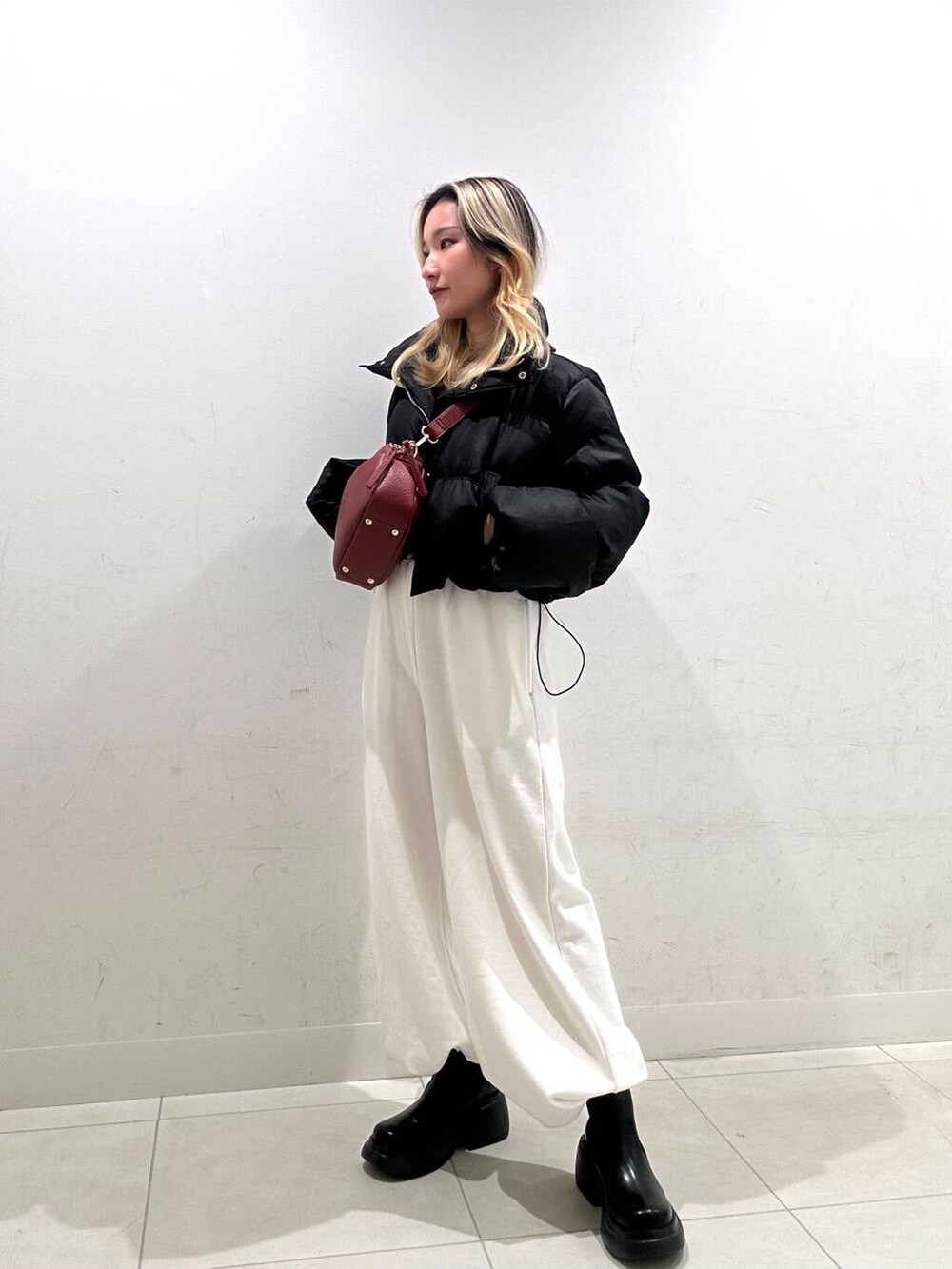 レッド系のショルダーバッグ、ブラック系のダウンジャケット/コート、ブラック系のブーツを着用したレディースの秋コーディネートの3枚目の写真