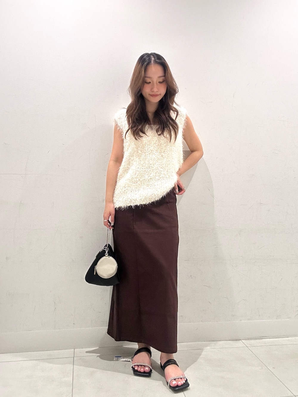 ホワイト系のベスト、ブラウン系のスカート、ブラック系のハンドバッグを着用したレディースの夏コーディネートの2枚目の写真