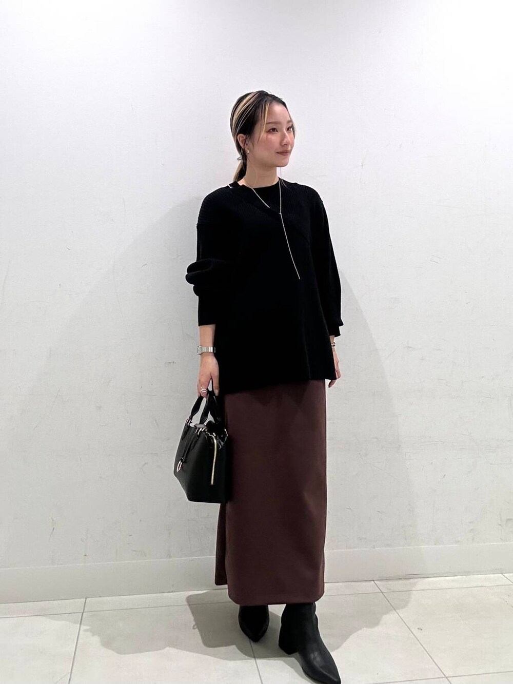 グレー系のノーカラーコート、ブラック系のハンドバッグ、ブラック系のニット/セーターを着用したレディースの冬コーディネートの2枚目の写真