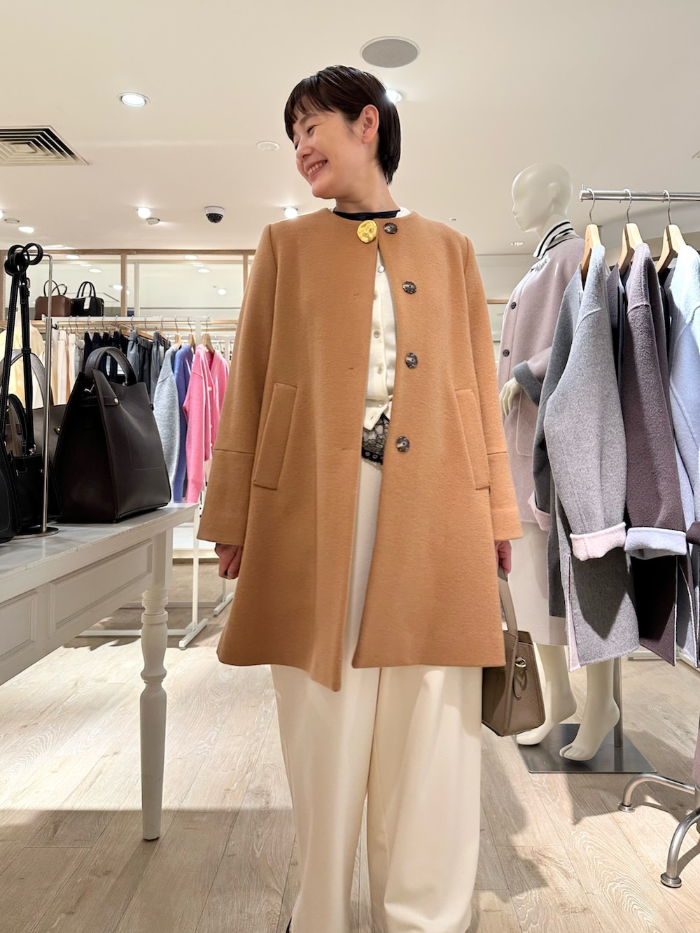 イエロー系のノーカラーコート、ホワイト系のカーディガン/ボレロ、ブラック系のシャツ/ブラウスを着用したレディースの冬コーディネートの2枚目の写真