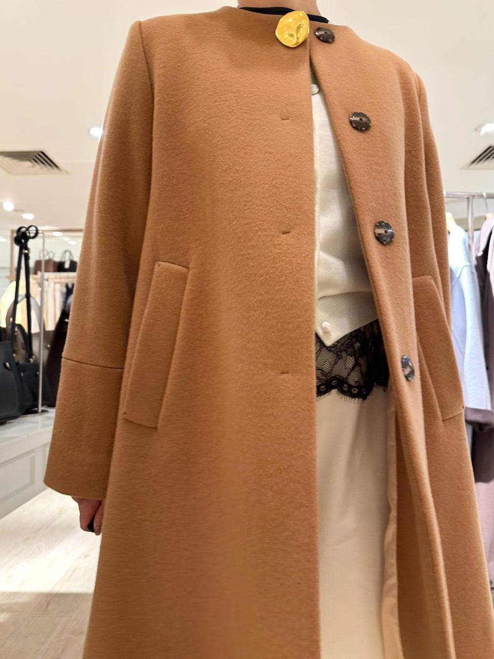 イエロー系のノーカラーコート、ホワイト系のカーディガン/ボレロ、ブラック系のシャツ/ブラウスを着用したレディースの冬コーディネートの9枚目の写真