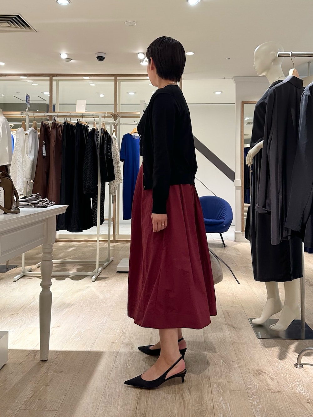 レッド系のスカート、ベージュ系のショルダーバッグ、ブラック系のニット/セーターを着用したレディースの秋コーディネートの2枚目の写真