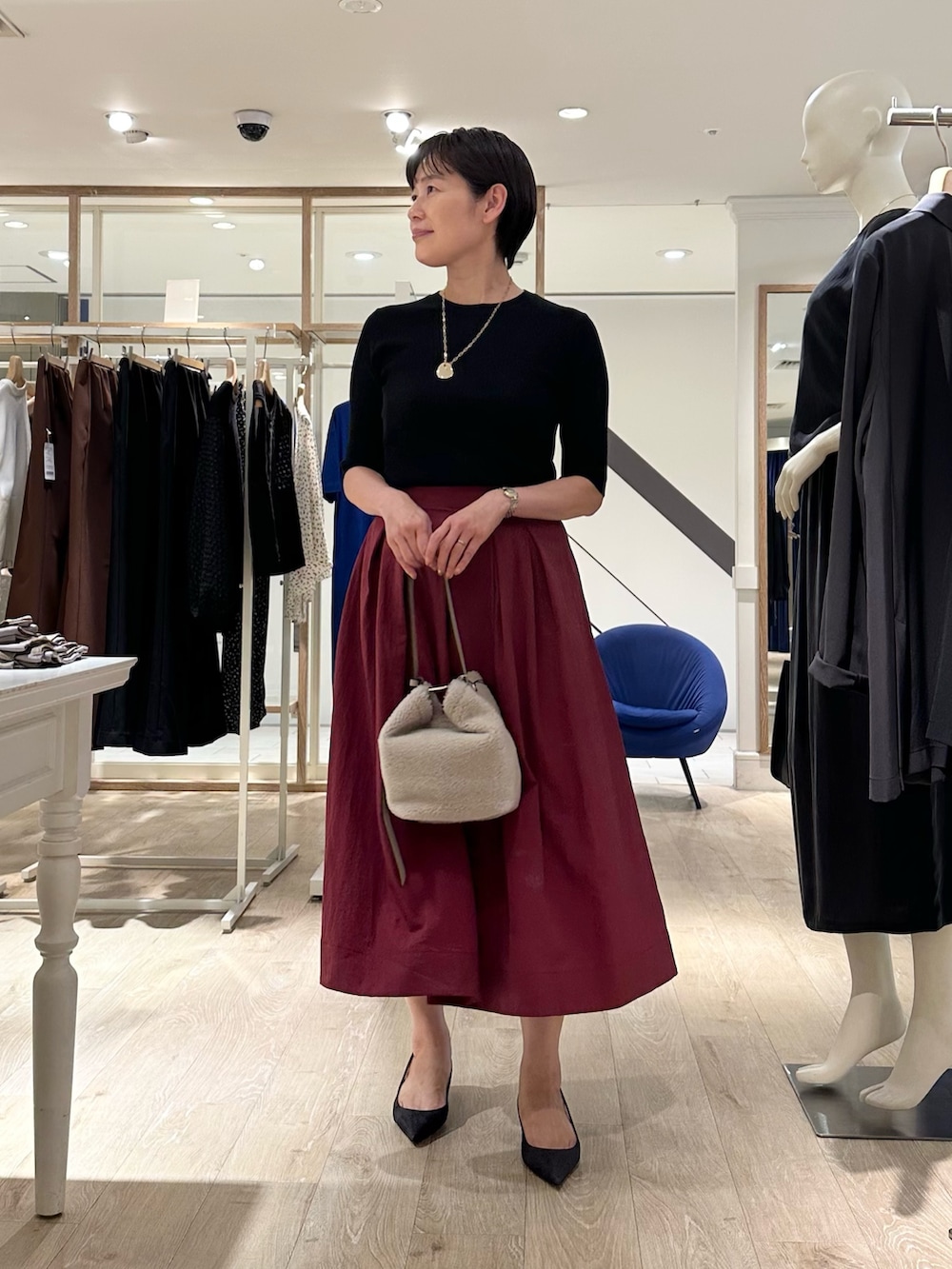 レッド系のスカート、ベージュ系のショルダーバッグ、ブラック系のニット/セーターを着用したレディースの秋コーディネートの6枚目の写真