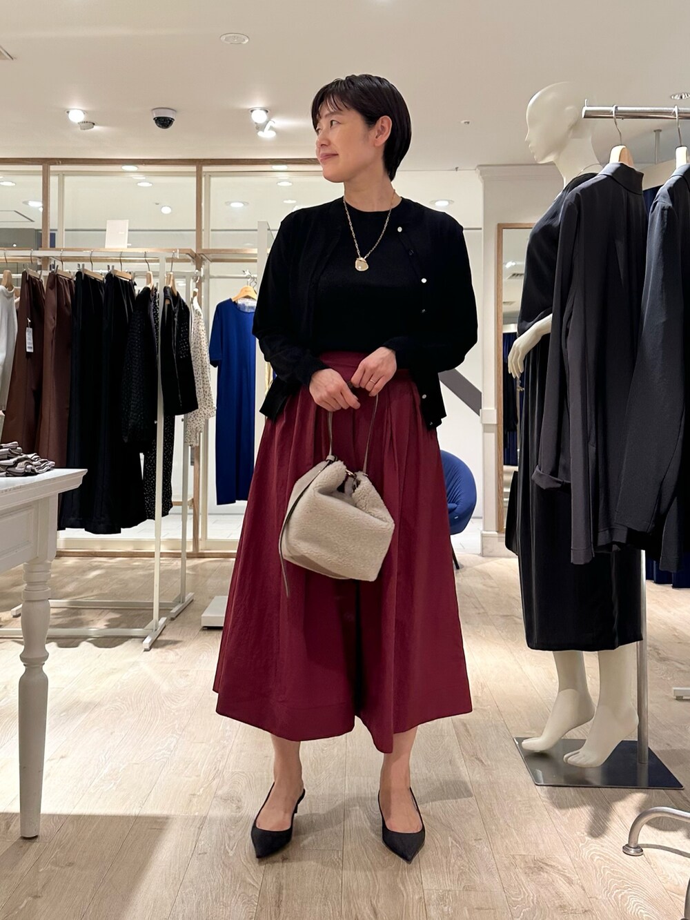 レッド系のスカート、ベージュ系のショルダーバッグ、ブラック系のニット/セーターを着用したレディースの秋コーディネートの4枚目の写真