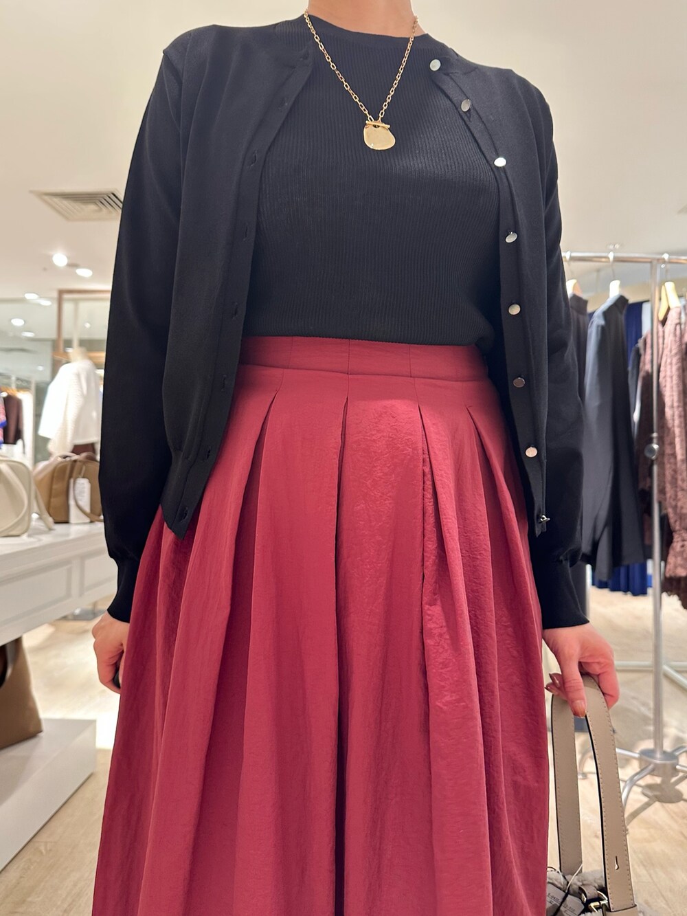 レッド系のスカート、ベージュ系のショルダーバッグ、ブラック系のニット/セーターを着用したレディースの秋コーディネートの5枚目の写真