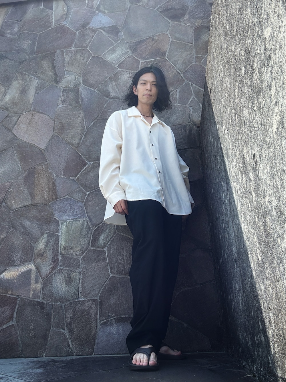 ブラック系のスラックス、ブラウン系のサンダル、ホワイト系のシャツ/ブラウスを着用したメンズの夏コーディネートの2枚目の写真