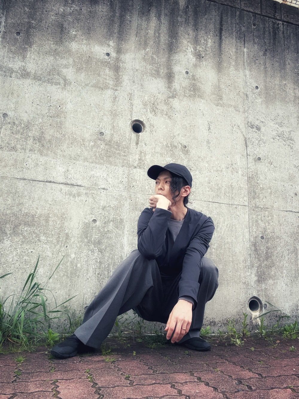 グレー系のスラックス、ブラック系のその他シューズ、ブラック系のノーカラージャケットを着用したメンズの春コーディネートの2枚目の写真