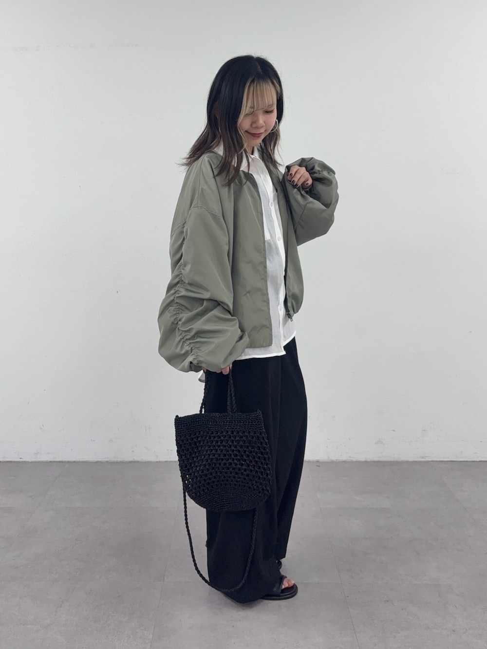 ブラック系のスラックス、ブラック系のショルダーバッグ、グリーン系のブルゾンを着用したレディースの春コーディネートの2枚目の写真