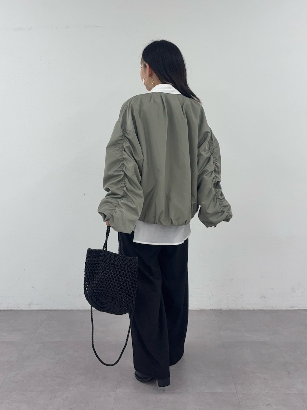 ブラック系のスラックス、ブラック系のショルダーバッグ、グリーン系のブルゾンを着用したレディースの春コーディネートの3枚目の写真