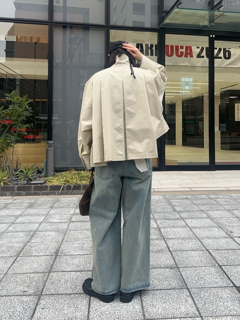 グレー系のステンカラーコート、ブラウン系のショルダーバッグ、ブルー系のデニムパンツを着用したレディースの冬コーディネートの2枚目の写真