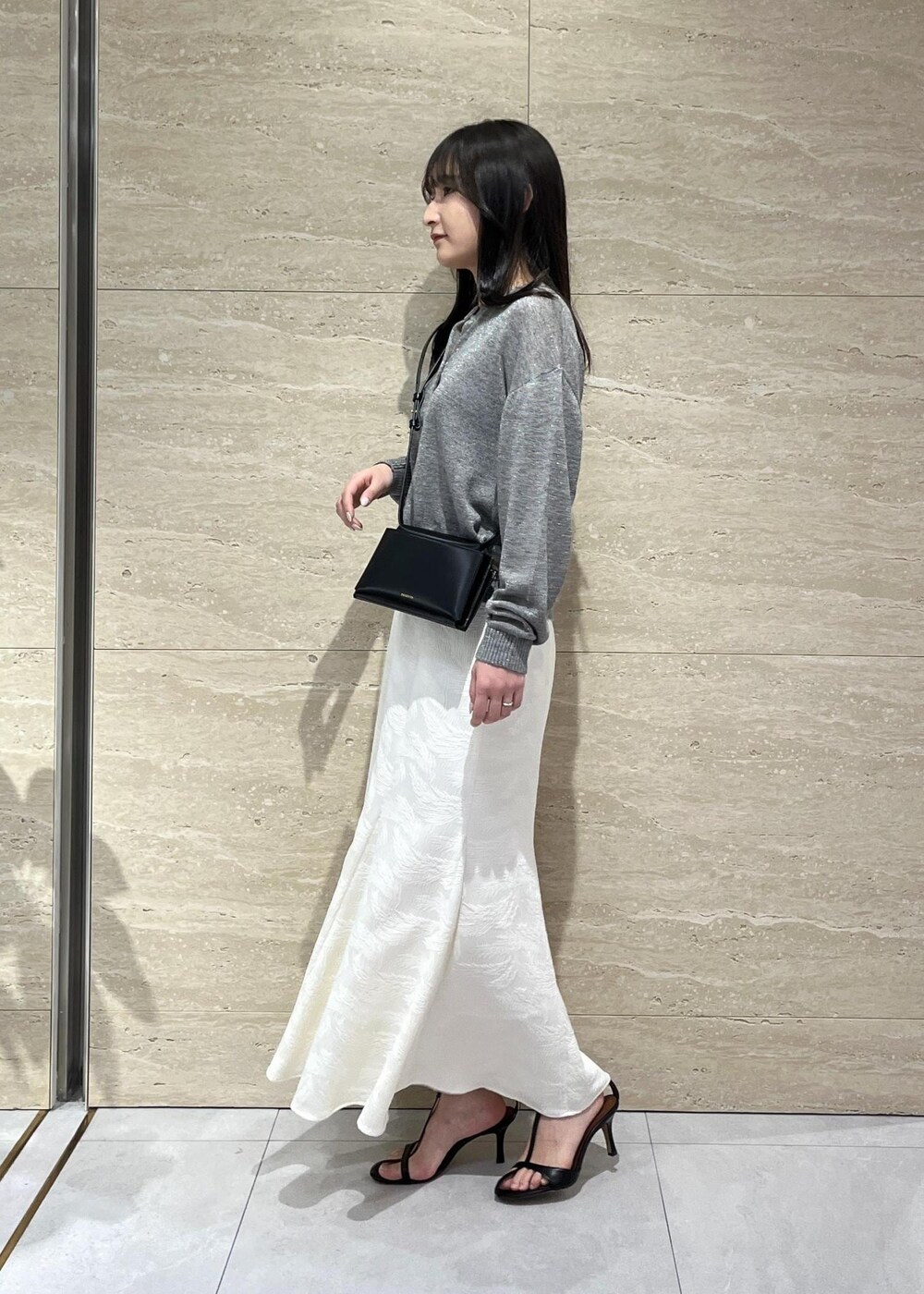 グレー系のカーディガン/ボレロ、ブラック系のサンダル、ホワイト系のスカートを着用したレディースの春コーディネートの2枚目の写真