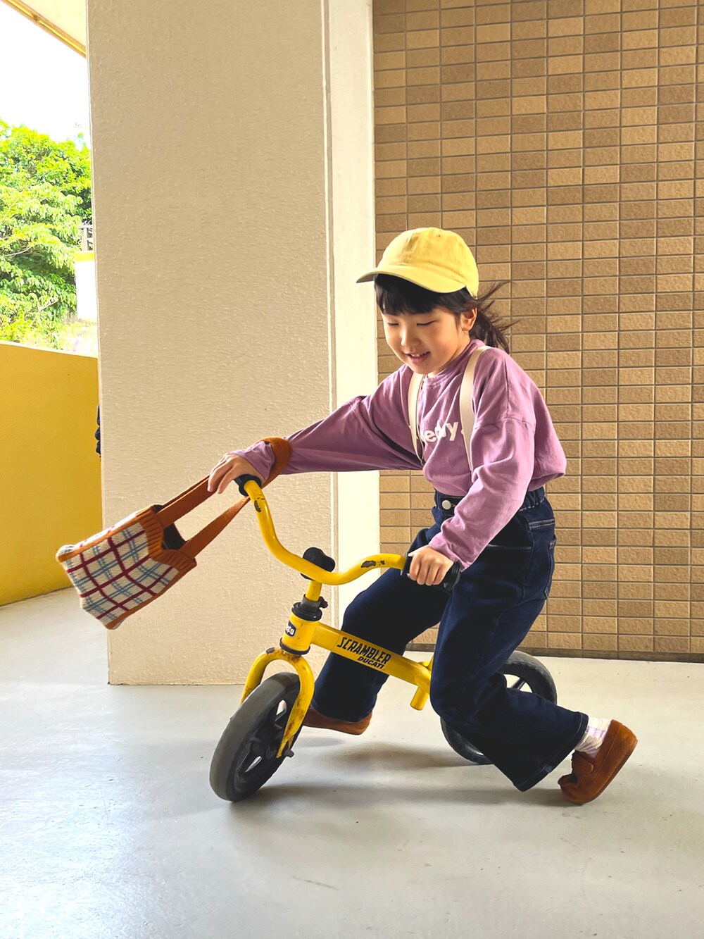 オレンジ系のトートバッグ、パープル系のTシャツ/カットソー、ブルー系のデニムパンツを着用したキッズの春コーディネートの2枚目の写真