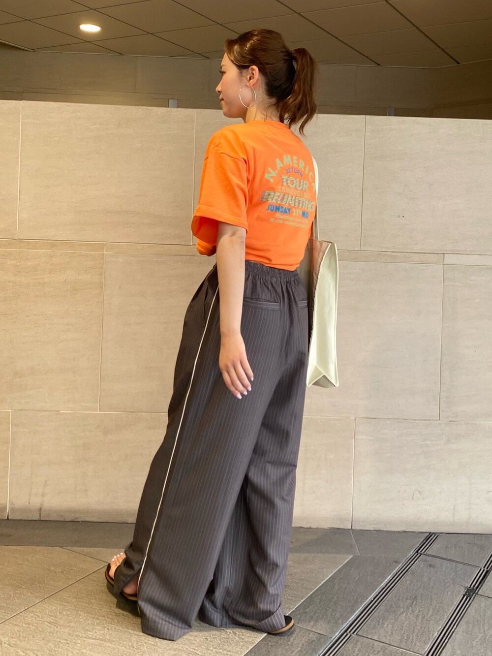 グレー系のその他パンツ、オレンジ系のTシャツ/カットソー、ホワイト系のトートバッグを着用したレディースの夏コーディネートの2枚目の写真