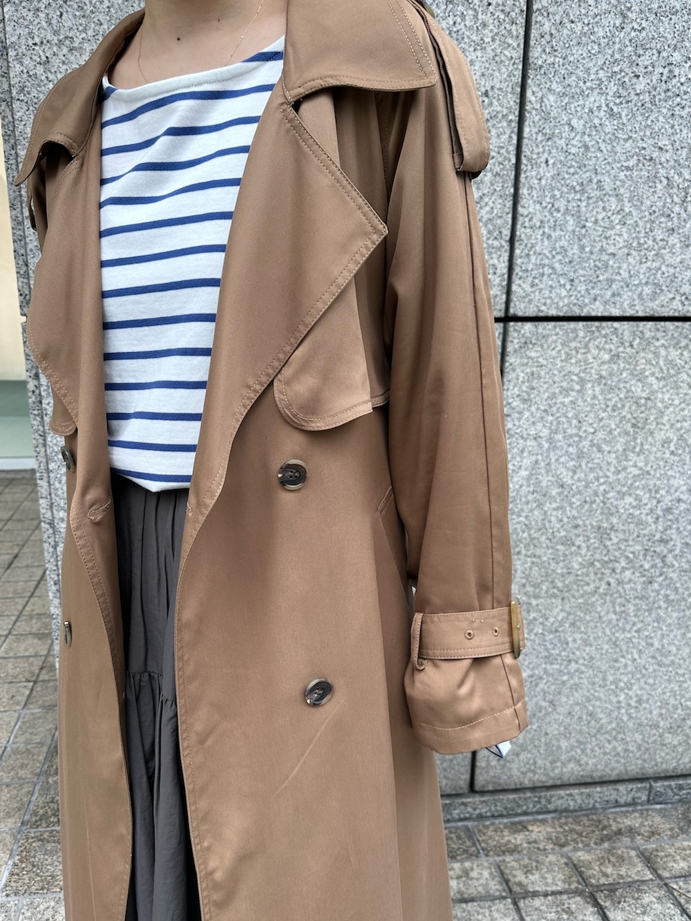 グレー系のスカート、オレンジ系のTシャツ/カットソー、ブラウン系のトレンチコートを着用したレディースの冬コーディネートの3枚目の写真