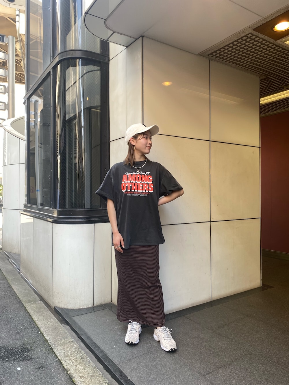 グレー系のTシャツ/カットソー、ブラウン系のワンピース、ホワイト系のキャップを着用したレディースの春コーディネートの2枚目の写真