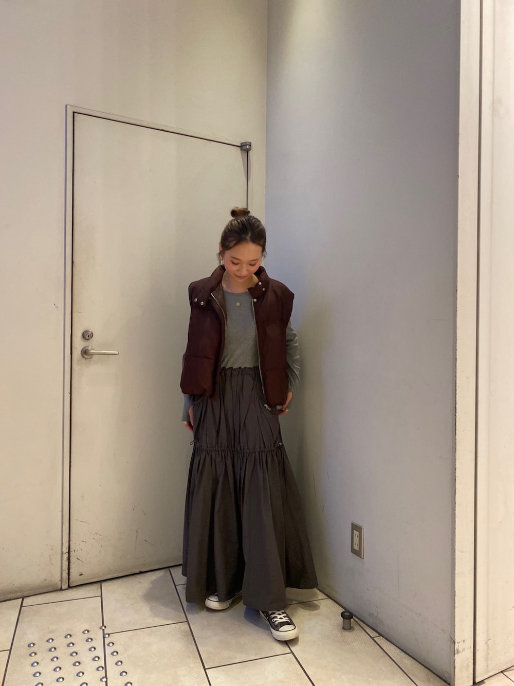 グレー系のワンピース、ブラウン系のダウンベストを着用したレディースの秋コーディネートの2枚目の写真