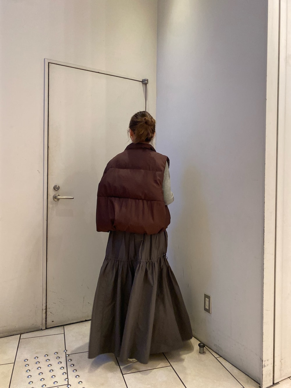 グレー系のワンピース、ブラウン系のダウンベストを着用したレディースの秋コーディネートの4枚目の写真