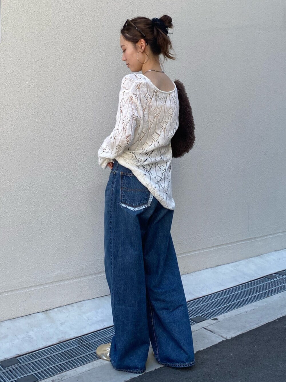 ブルー系のデニムパンツ、ホワイト系のニット/セーター、ブラウン系のハンドバッグを着用したレディースの夏コーディネートの2枚目の写真