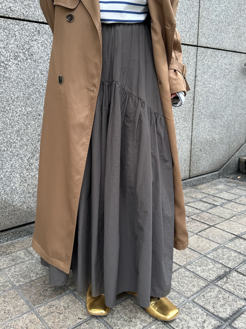 グレー系のスカート、オレンジ系のTシャツ/カットソー、ブラウン系のトレンチコートを着用したレディースの冬コーディネートの4枚目の写真