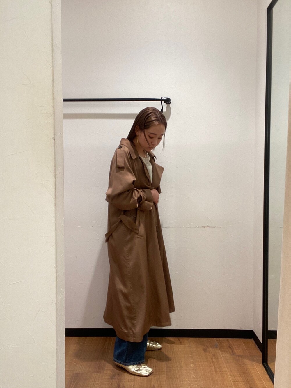 イエロー系のトレンチコート、ブルー系のデニムパンツ、ゴールド系のパンプスを着用したレディースの春コーディネートの3枚目の写真