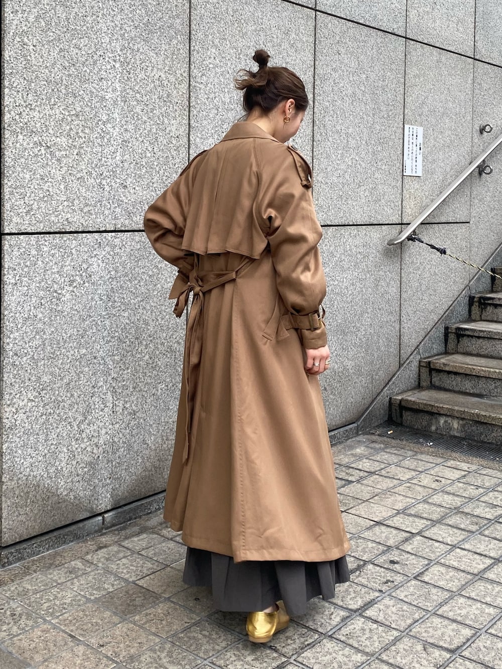 グレー系のスカート、オレンジ系のTシャツ/カットソー、ブラウン系のトレンチコートを着用したレディースの冬コーディネートの2枚目の写真