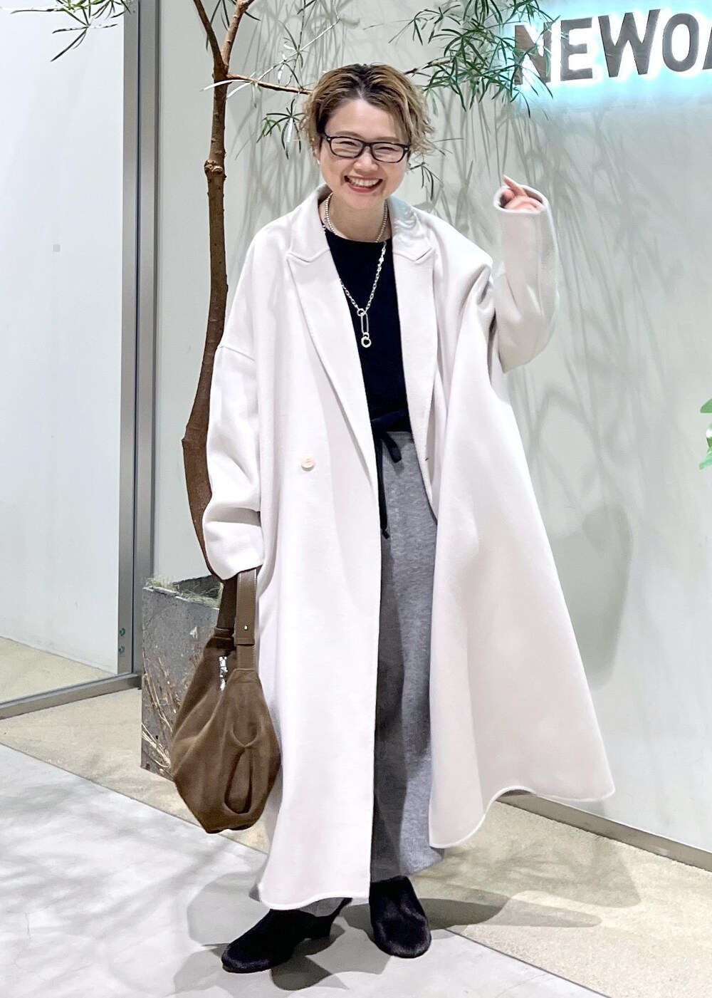 ホワイト系のチェスターコート、ブラック系のスウェット、ブラウン系のショルダーバッグを着用したレディースの秋コーディネートの2枚目の写真